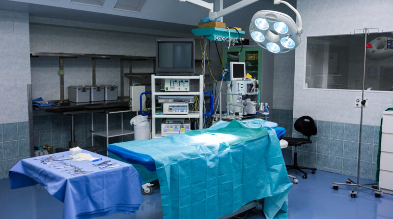 Vista de sala de cirurgia composta por uma maca, itens de bisturi e equipamentos cirúrgicos